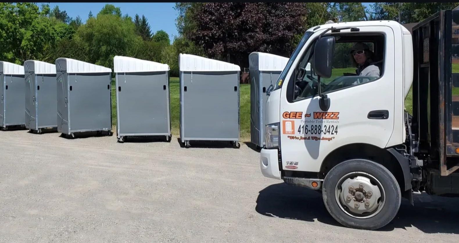 Gee Wizz delivery truck beside a row of portable toilet units ready for delivery